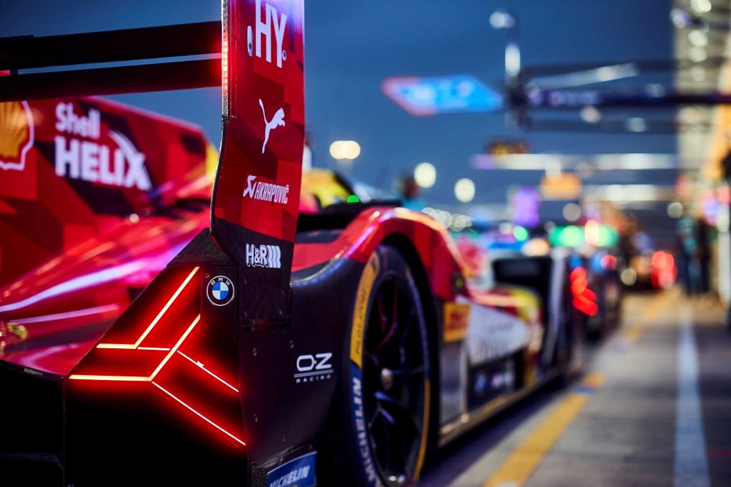 Auto de competicion BMW en los boxes durante una carrera nocturna con branding de Shell Helix en el aleron trasero