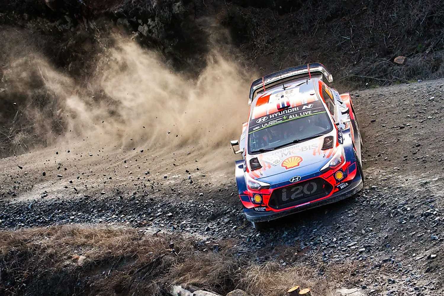 Coche de rally Hyundai i20 WRC patrocinado por Shell tomando una curva en un tramo de tierra levantando polvo durante una competicion del World Rally Championship