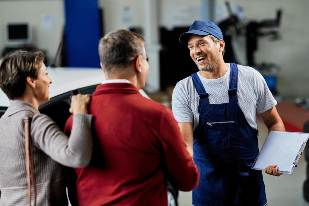 Mecánico saludando a clientes satisfechos, destacando la confianza y el servicio cercano de Shell Lubricants Mecánico saludando a clientes satisfechos, destacando la confianza y el servicio cercano de Shell Lubricants